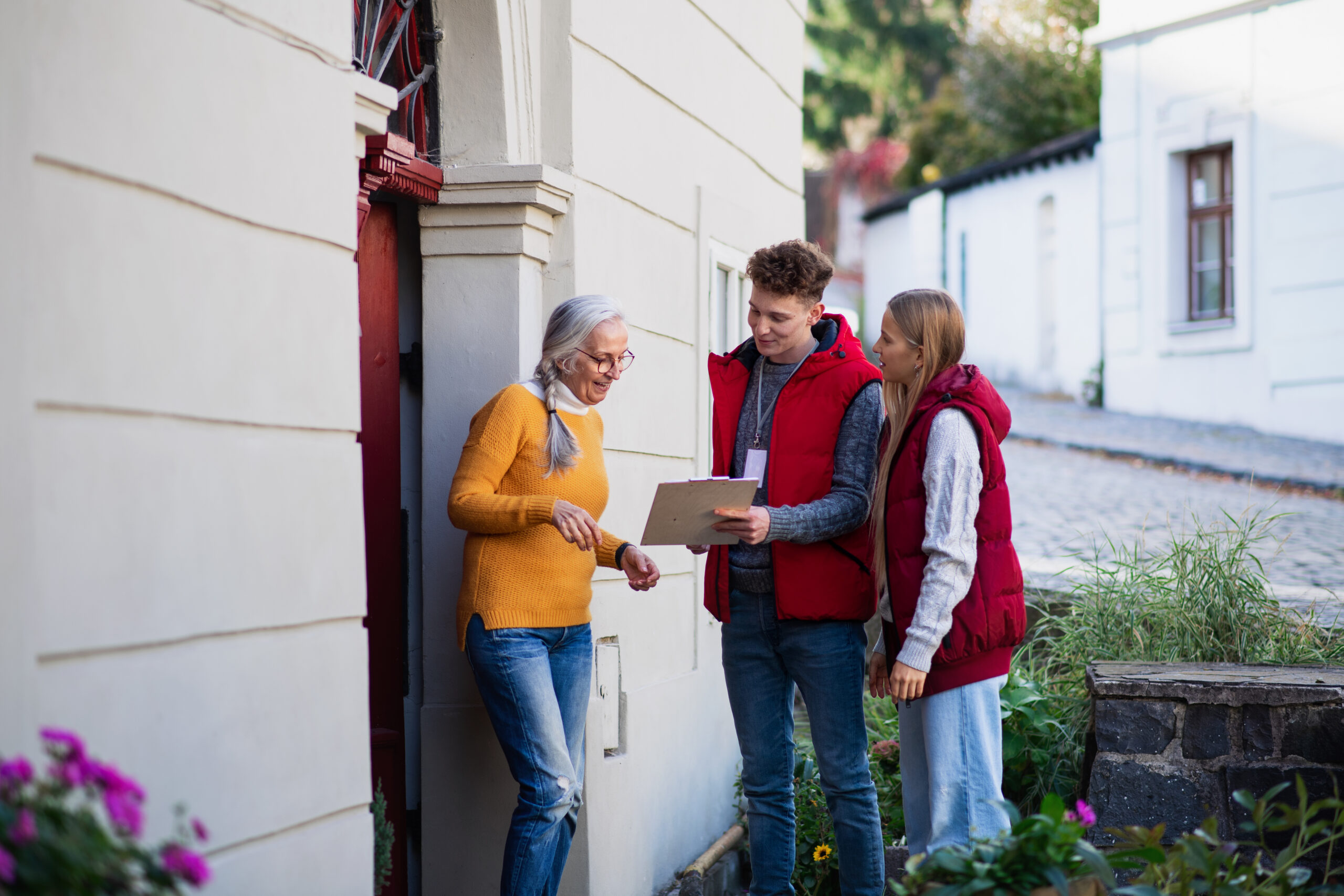 Young door to door volunteers talking to senior woman and taking survey at her front door.